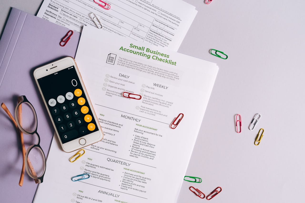 hero-img-02 Top view of accounting essentials including smartphone, eyeglasses, and paperwork.